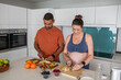 © wavebreak3 - Diverse couple in sportswear slicing fruit on cutting boards in home kitchen next to blender base