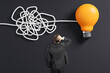 © Who is Danny - Businessman looking at tangled wire turning into lightbulb symbol on dark background, representing problem-solving and creative thinking.
