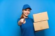 © luismolinero - Delivery girl over isolated blue wall pointing front with happy expression