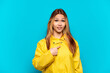 © luismolinero - Teenager girl wearing a rainproof coat over isolated blue background with surprise facial expression