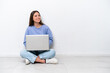 © luismolinero - Young caucasian woman with laptop sitting on the floor isolated on white background laughing in lateral position