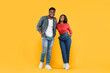 © Prostock-studio - Two people stand next to each other in a bright yellow setting. They smile while dressed in casual clothing. The man wears a checkered shirt and jeans, while the woman wears a red top and blue jeans.