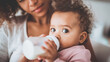 © Bonsales - Loving mother feeding her adorable African American baby milk from a bottle, creating a bond during care time