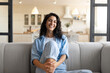 © Prostock-studio - Portrait of pretty young brunette woman smiling and looking at camera, sitting on couhc at home. Caucasian millennial female model expressing joy and happiness. Positive emotions concept