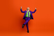 © deagreez - Elderly man in vibrant purple suit dances joyfully against bright orange background wearing green shirt green tie and sunglass
