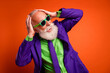 © deagreez - Vibrant retro style man in purple suit and green shirt posing playfully against a bright orange background