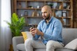 © Liubomir - Young man relaxing on couch browsing internet on mobile phone, staying connected with digital technology, social media, and online communication in a comfortable living room