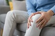 © Liubomir - Middle-aged man sitting on a couch pressing his painful knee, grimacing from joint ache and inflammation, suggesting injury, arthritis or need for medical attention and treatment
