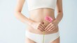 © Eve - A slender woman in white lingerie holding a pink gerbera flower in front of her stomach, concept for female wellness, menstruation, digestive health, and beauty care, studio shot.