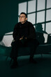 © Alex May - A portrait photo of a male model in a dark studio with window light. The handsome man wearing glasses looks into the camera. The businessman and his fashionable, elegant style