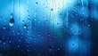 © Bucek - Close-up abstract view of vivid blue water droplets streaming down a wet window surface.