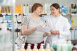 © JackF - Mature woman holds a medical prescription with a description of medicines and she consults a pharmacist at a pharmacy