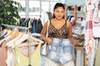 © JackF - Latin woman in summer clothes chooses denim shorts against the background of the interior of the store. Cuban looking at comfortable denim shorts