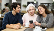 © JackF - Family of different ages in cafe will scroll through photo albums and social networks. Grandchildren help their grandmother use her smartphone and social media.