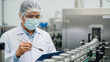 © Bakha - Quality control technician inspecting metal cans on automated beverage production line in modern factory wearing protective mask, safety glasses, hairnet and lab coat checking data on clipboard