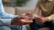 © Curioso.Photography - Person gesturing with open hands during a therapy or counseling session in a calm indoor setting.