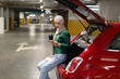 © Sofiia Shunkina - A woman wearing a hijab sits in the open trunk of a red car, looking at her phone while holding a coffee cup