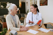 © AnnaStills - Caucasian senior woman listening to young adult Caucasian female doctor explaining medication instructions while holding pill bottle during medical consultation at home