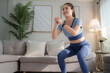 © crizzystudio - Young woman enjoying home workout doing squats