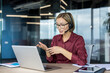 © Liubomir - Businesswoman with glasses and headset having a video call discussion, gesturing with hands during an online meeting or customer service interaction using a laptop in a modern office