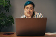 © Lomb - Frustrated non-binary student with blue hair looking at laptop screen during online education class at home
