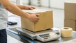 © adaptable_ Lark98A1 - A person weighing a cardboard box on a scale in a shipping area, preparing it for dispatch or delivery.