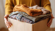 © Annamorphosis - Person holding a box of donated clothes with compassion