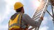 © Bussakon - A construction worker wearing a yellow hard hat and safety vest is ascending a tall metal ladder against a bright sky