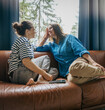 © olezzo - Lesbian couple cuddling on sofa at home, LGBT family and Valentine’s Day concept
