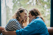 © olezzo - Lesbian couple sitting face to face on sofa touching each other’s faces, intimate moment at home