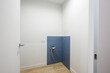 © evgeniykleymenov - Small bathroom corner with blue tiled niche, exposed plumbing, white walls, wooden floor, electrical outlet, modern door with sleek handle — minimalist setup.