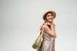 © Volodymyr_sh - Smiling young woman in straw hat and summer dress carrying reusable mesh shopping bag with vegetables on light background