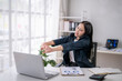 © Wasana - Businesswoman stretching arms at office desk with laptop