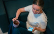 © M-Production - Woman holding cup and using smartphone indoors.