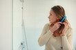 © M-Production - Young woman combing her hair in bathroom.