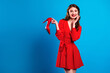 © deagreez - Young woman in red polka dot dress holds red heel smiling against blue background for fashion lifestyle and shopping promo