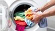 © CreativeArt - Hands putting colorful clothes into a washing machine, performing a common household chore. Laundry