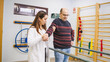 © DMegias - Physiotherapist aiding a male patient with a long term physical condition, emphasizing assisted walking and recovery in a clinic