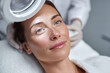 © EricMiguel - Relaxed woman receiving facial examination under magnifying lamp at a skincare clinic, glowing complexion and serene expression during beauty treatment