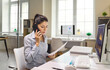 © Studio Romantic - Woman advisor on phone call with client. She reads documents at a computer in the office, discussing investments, loans and interest rates for decisions. Finance advice and support concept.