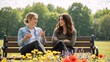 © Vasiliy - Two young women friends talking and smiling on a park bench. Happy female couple having a friendly conversation outdoors on a sunny day