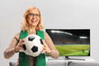 © Ljupco Smokovski - Mature woman in front of tv and sofa holding a football