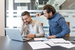 © Liubomir - Aggressive executive is shouting and pointing at a frustrated male employee working on a laptop, depicting workplace conflict, stress, and a tense business environment