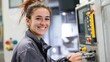 © mila103 - A young woman smiles while using a control panel in a workshop. She wears safety gear and appears focused on her work showcasing a blend of professionalism and enthusiasm.