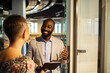 © Marko Geber - Smiling businessman greeting coworker with tablet in modern office