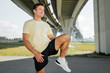 © muse studio - Man stretches his leg under a bridge before running in an outdoor area during daytime
