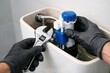 © Aleksandra - Plumber repairing toilet flush mechanism with adjustable wrench and gloves, fixing water tank valve for bathroom maintenance