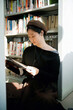 © zhouyilu - Young Woman Reading Book in Library Amid Bookshelves
