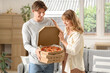 © Pixel-Shot - Beautiful young couple holding cardboard boxes with tasty pizza in living room