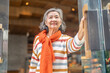 © Art_Photo - Happy senior asian woman pushing glass door entering cafe, smiling elderly lady with orange scarf enjoying city lifestyle, active retirement, customer, small business and welcome concept